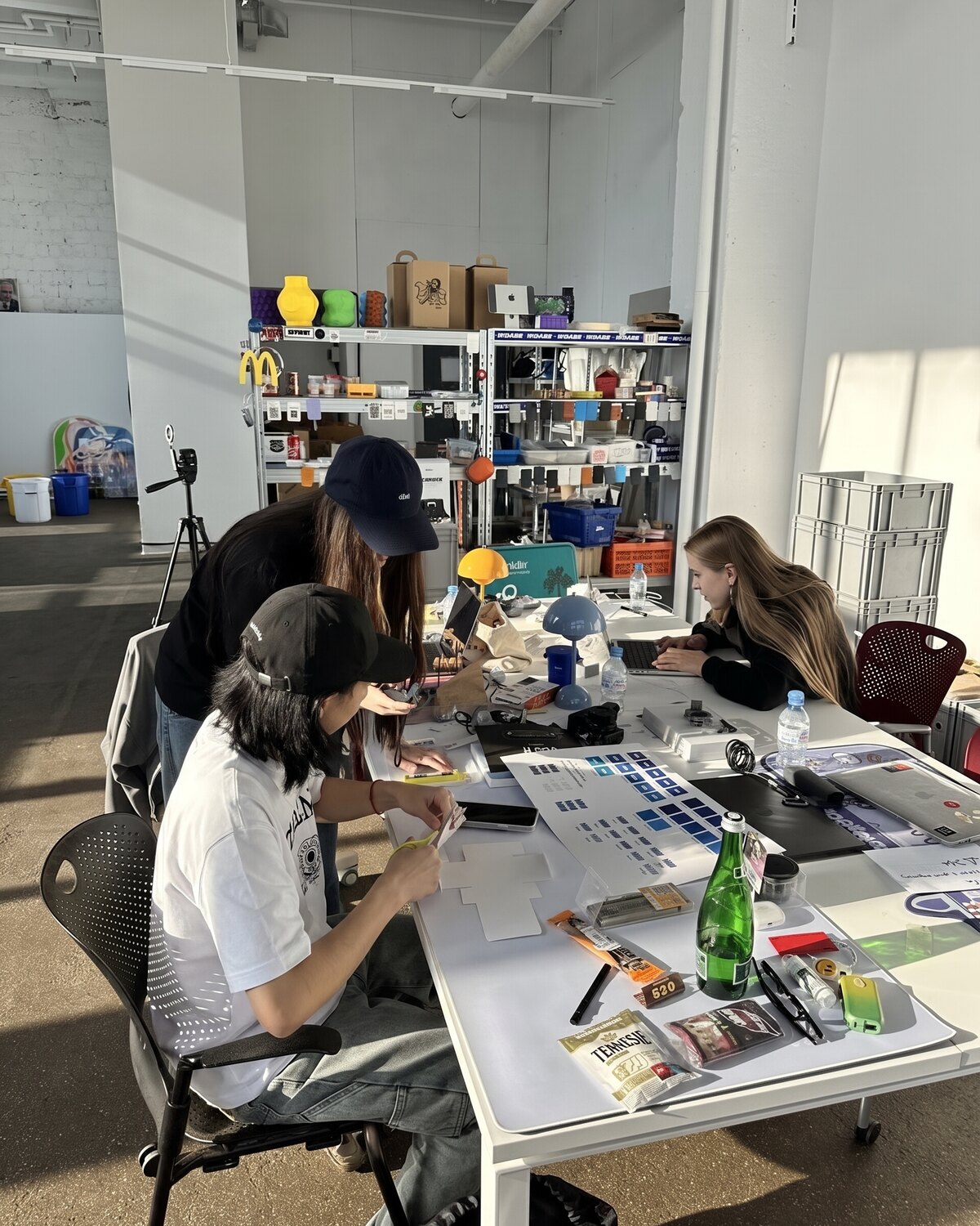 A studio work session: three people at a table with models, colour swatches and materials