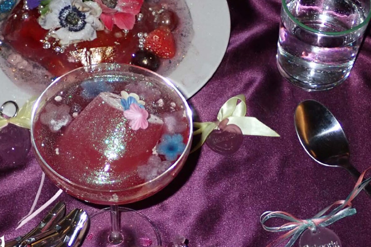 A dessert set on purple silk: a jewelled coupe glass and a cake studded with flowers and edible stones